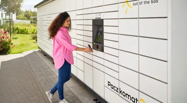 Kobieta z telefonem przy Paczkomacie InPost. Szybka wysyłka paczek za granicę jest teraz prosta.