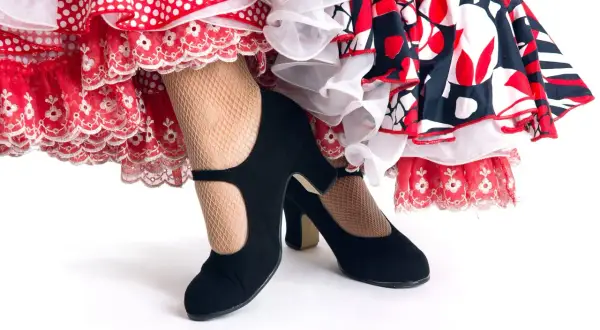 Zapatos negros de tacón y medias de rejilla, listos para el zapateo flamenco entre volantes de lunares y encaje.