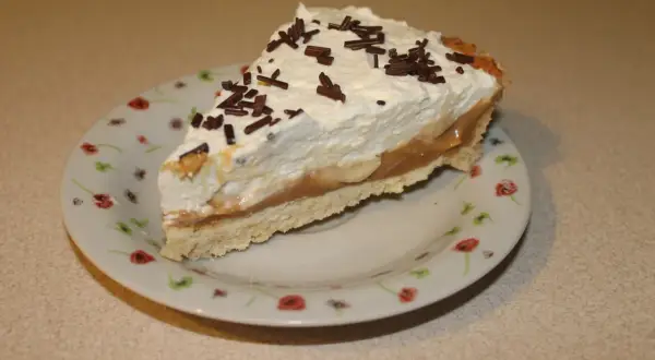 Pyszna tarta bananowa z bitą śmietaną i czekoladową posypką, podana na talerzyku w kwiatki.