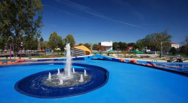 Nowoczesny park bajka w Błoniu z fontanną i niebieską nawierzchnią, idealny na letnie zabawy.