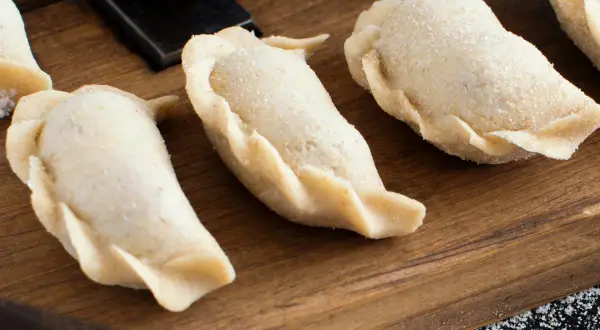 Surowe pierogi na desce. Zastanawiasz się, ile gotować pierogi, by były idealne?