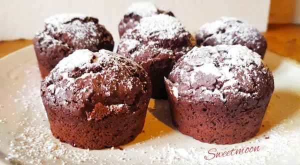 Cinque muffin al cioccolato senza burro, spolverati di zucchero a velo, su un piatto chiaro.
