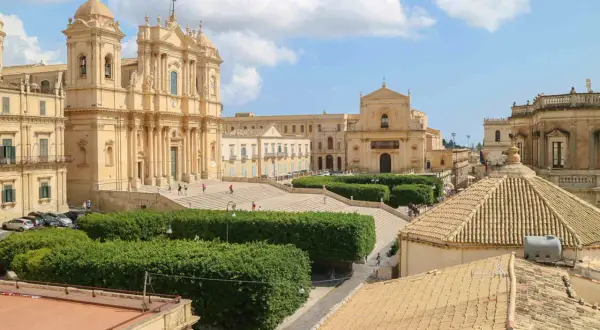 Piazza barocca con chiese imponenti e giardini curati, un esempio di città d'arte Italia sotto un cielo azzurro con nuvole bianche.