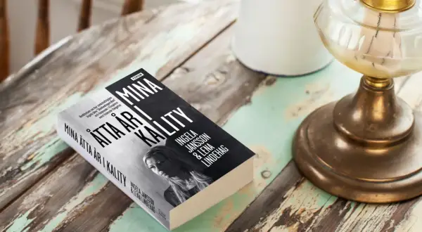 Boken "Mina åtta år i kalitet" av Ingela Jansson och Lena Lindehag ligger på ett slitet träbord.