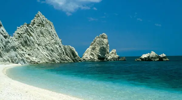 Spiaggia bianca e mare cristallino, rocce imponenti emergono dall'acqua turchese. Un angolo di paradiso nelle Marche, mare bello da cartolina.