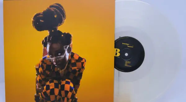 Little Simz, czasem introvert, na okładce płyty "Sometimes I Might Be Introvert". Obok przezroczysta winylowa płyta.