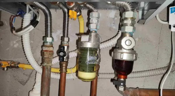Manutenzione caldaia: pulizia filtro defangatore. Si vedono tubi, valvole e due filtri, uno con liquido giallo e uno con liquido scuro.