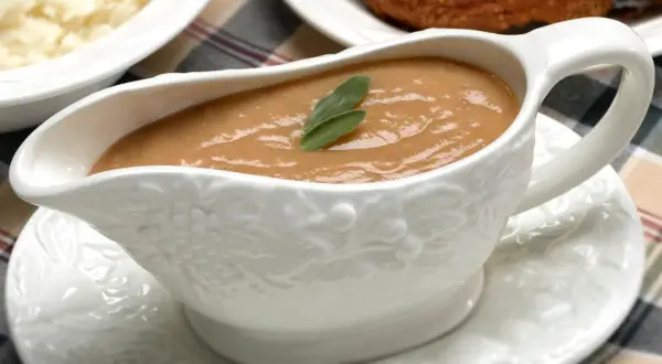Saucière en porcelaine ornée de grappes de raisin, remplie d'une onctueuse sauce foie gras, garnie d'une feuille de sauge.