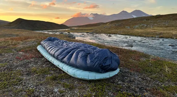 Sovsäck och liggunderlag redo för en natt i fjällen. Test av liggunderlag vid en forsande älv i solnedgången.