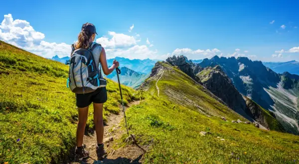 Une randonneuse admire le panorama spectaculaire des Alpes françaises. Le sentier serpente à travers des prairies verdoyantes, offrant une vue imprenable sur les montagnes majestueuses.