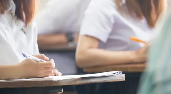 Dłoń studenta pisząca długopisem na kartce papieru podczas egzaminu.