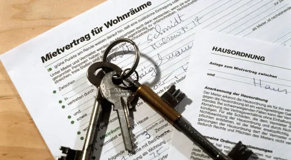 Schlüsselbund liegt auf einem Mietvertrag und einer Hausordnung. Der Text "Mietvertrag nicht unterschreiben" ist nicht direkt sichtbar, aber die Dokumente deuten auf eine Wohnungsanmietung hin.