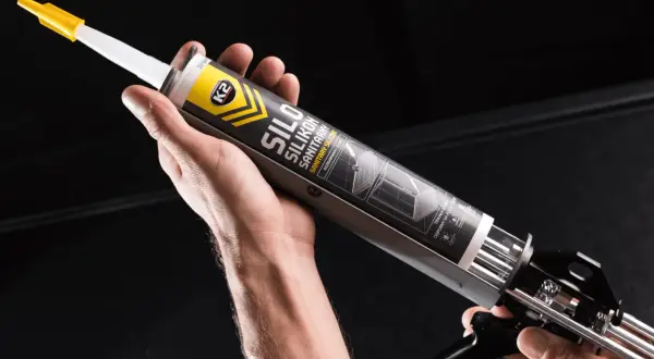 Dłoń trzyma pistolet z tubą silikonu sanitarnego K2. Czy można kłaść silikon na nowy silikon? Ten produkt pomoże Ci to sprawdzić.