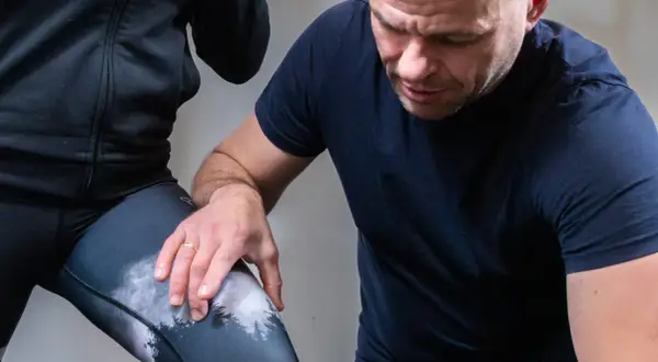 Fizjoterapeuta sprawdza kolano biegacza podczas ćwiczeń rehabilitacyjnych.