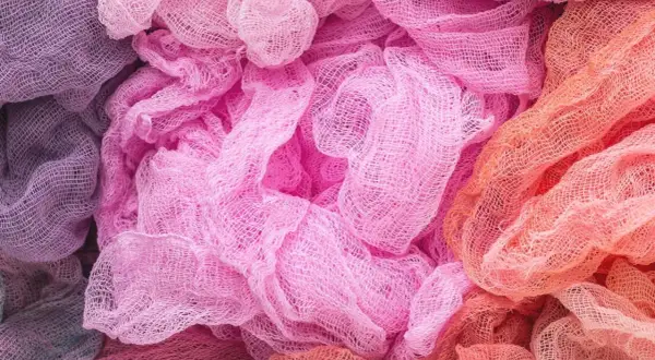 Tessuti morbidi e drappeggiati in tonalità pastello, dal lilla al rosa acceso fino all'arancio. Un'ispirazione per chi vuole imparare come decolorare un tessuto e creare sfumature uniche.