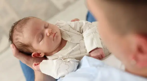 Un neonato dorme sereno tra le braccia di un genitore, cullato dal dolce rumore bianco che favorisce il sonno.