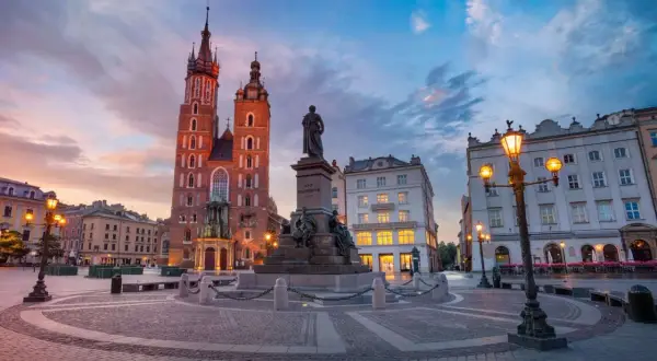 Krakowski rynek główny o zachodzie słońca. Monumentalna Bazylika Mariacka i pomnik Adama Mickiewicza w blasku latarni.
