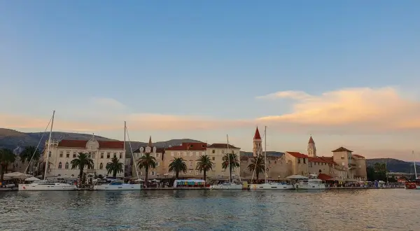Trogir co zobaczyć: malownicza starówka z palmami i żaglówkami przy nabrzeżu, w blasku zachodzącego słońca.