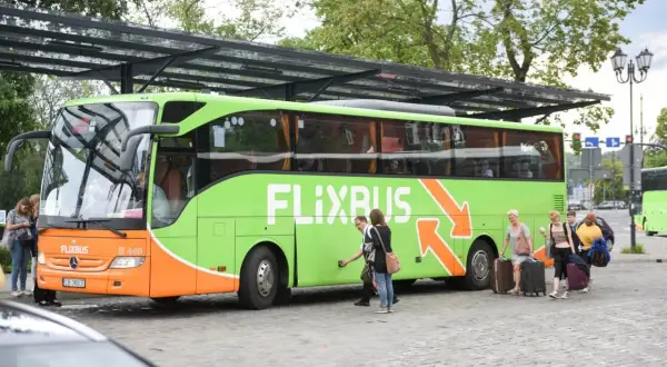 Zielony autobus Flixbus z pasażerami i bagażami na przystanku.