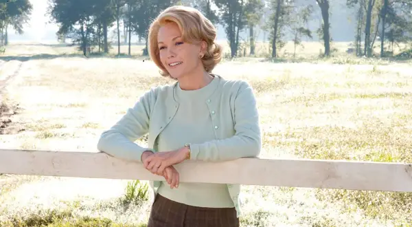 Diane Lane w pastelowym sweterku opiera się o płotek, przypominając scenę z jednego z jej filmów.