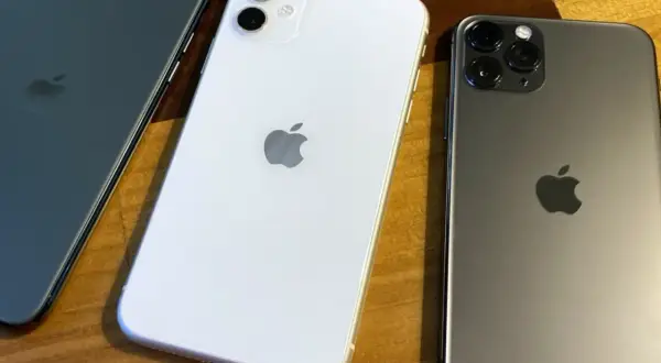 Trois iPhones 11, blanc et gris, sur un fond en bois. La date de sortie de l'iPhone 11 était le 20 septembre 2019.