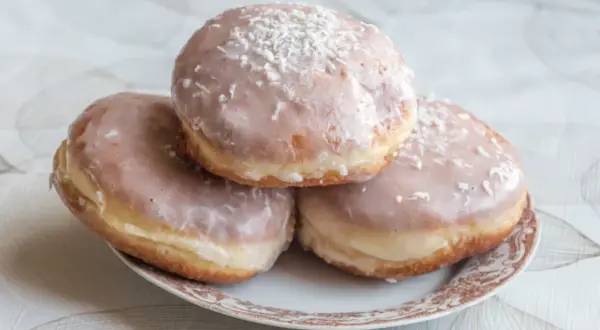 Trzy pączki z lukrem do pączków i wiórkami kokosowymi na talerzyku.