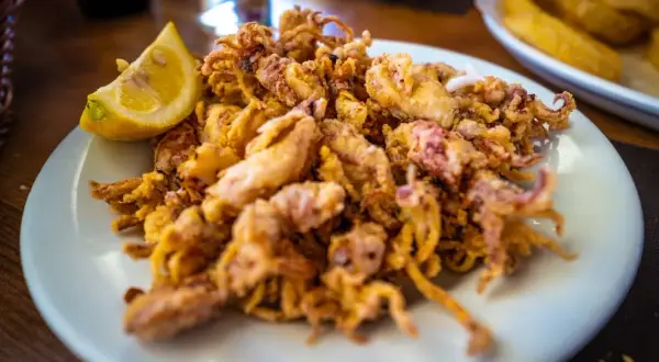 Un plato de puntillas de calamar fritas, doradas y crujientes, con un gajo de limón.