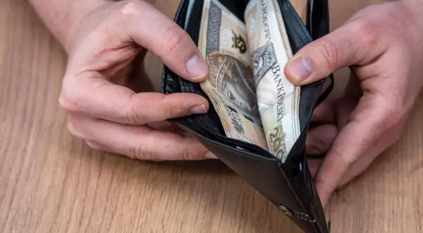 Dłonie trzymające otwarty portfel z polskimi banknotami.