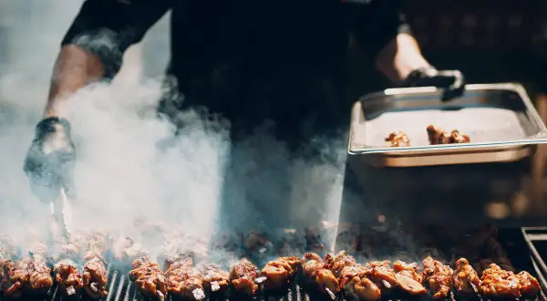 Fleischspieße brutzeln auf dem Grill, Rauch steigt auf. Ein Koch bereitet ein italienisches Grillfest vor.