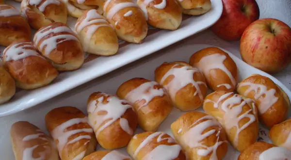 Pyszne pierogi z jabłkami, polane lukrem, kuszą swoim wyglądem. Obok leżą świeże jabłka.