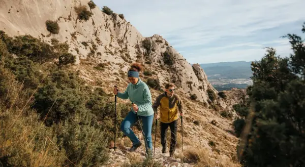 Deux randonneurs débutants progressent sur un sentier rocailleux, bâtons en main, sous un ciel bleu.