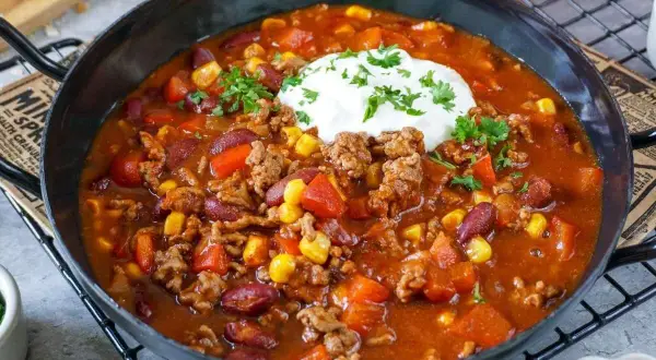 Herzhaftes Chili con Carne Rezept mit Hackfleisch, Kidneybohnen, Mais und Paprika, garniert mit einem Klecks Sour Cream und Petersilie.