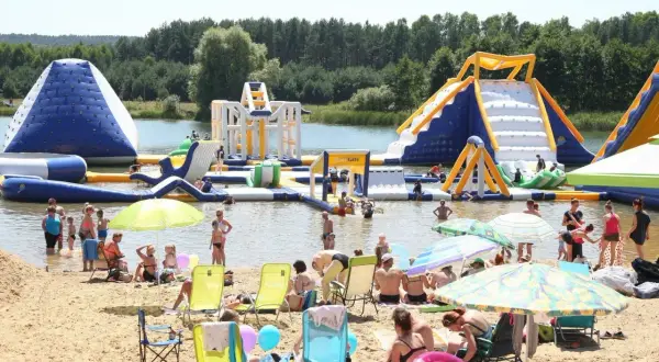 Ludzie bawią się na dmuchanych atrakcjach wodnych na **bolmin zalew**. Słoneczny dzień, plaża pełna wypoczywających.