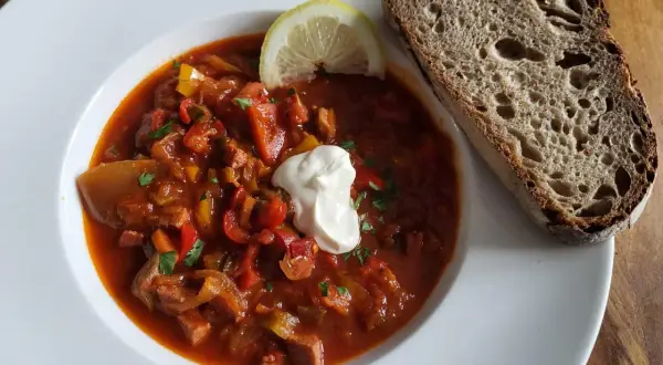 Herzhafte Soljanka, ein DDR-Rezept, mit saurer Sahne, Zitrone und Brot.