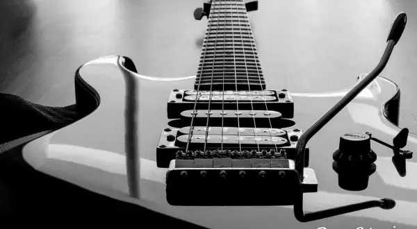 Czarno-białe ujęcie gitary elektrycznej z widocznym gryfem, strunami i przetwornikami. Napis "Drop C tuning" sugeruje specyficzne strojenie instrumentu.