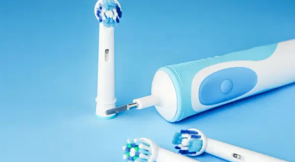 Spazzolino elettrico si accende da solo, pronto per l'igiene orale. Testine di ricambio su sfondo blu.