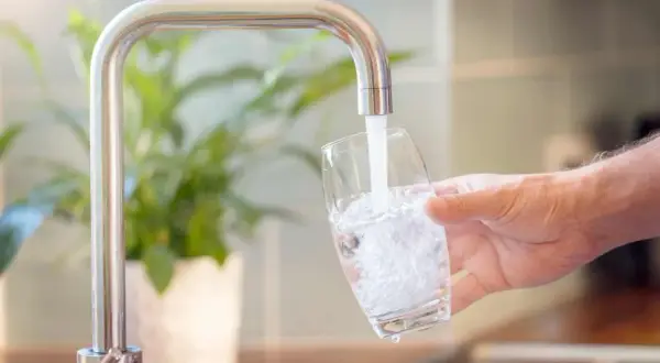 Un robinet verse de l'eau dans un verre, montrant comment obtenir de l'eau filtrée pour une boisson saine.