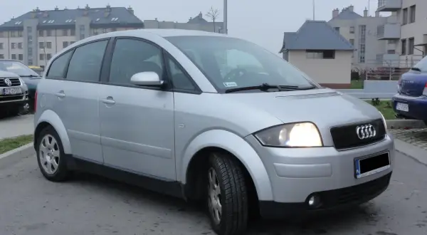 Srebrny Audi A2 1.4 benzyna zaparkowany przed blokami.