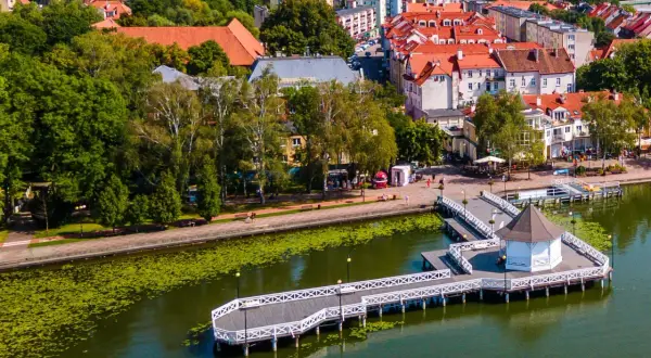Malownicza trasa w Ostródzie nad jeziorem z promenadą i altanką. W tle zabudowa miejska i zieleń.