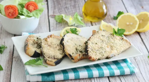 Fette di pesce spada in friggitrice ad aria, impanate con semi di sesamo e erbe aromatiche, servite con limone e insalata.