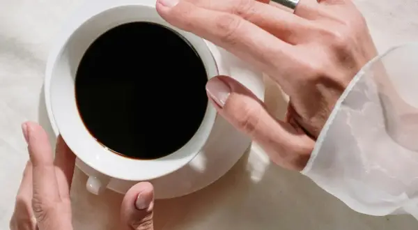 Händer som håller en kopp svart kaffe, en påminnelse om nackdelar med kaffe som sömnlöshet och oro.