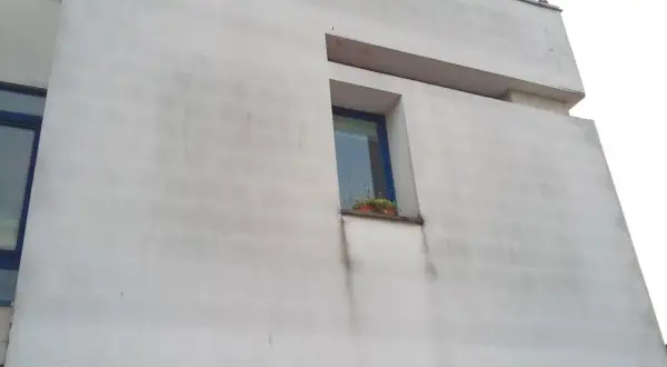 Facciata di un edificio con cappotto termico che mostra segni di muffa e macchie scure sotto la finestra.
