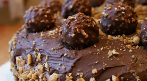 Pyszny tort oblany czekoladą, ozdobiony całymi pralinami i posypany orzechami. Wygląda jak idealny krem Ferrero Rocher.