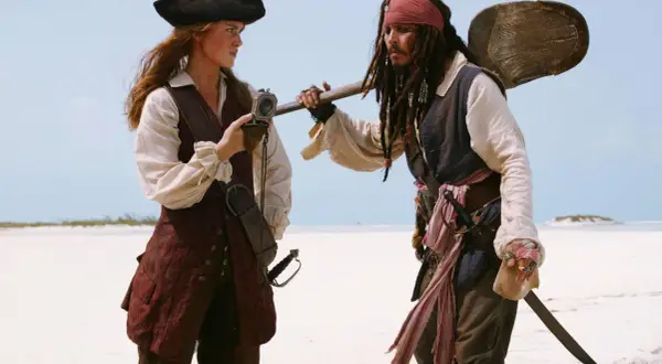 Elizabeth Swann i Kapitan Jack Sparrow, bohaterowie filmów "Piraci z Karaibów", stoją na piaszczystej plaży.