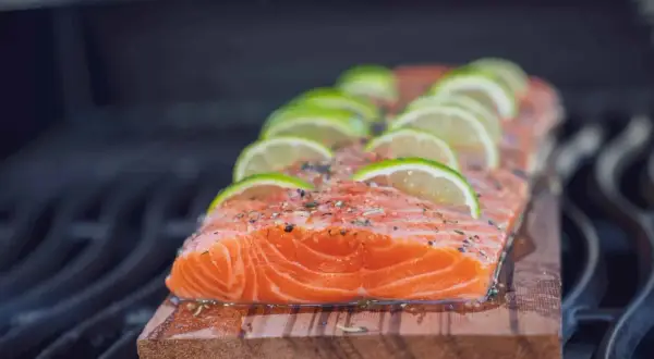 Ein saftiges Lachsfilet mit Limettenscheiben und Kräutern wird auf einem Zedernholzbrett gegrillt.