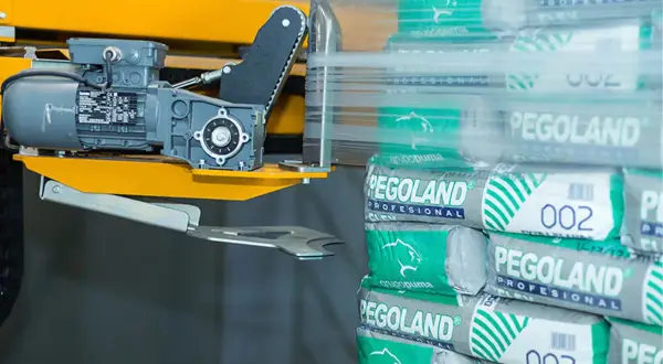 Paleta worków cementu Pegoland owinięta folią, obok maszyna pakująca.