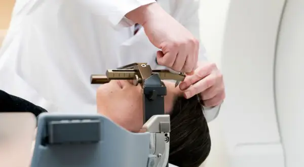 Arzt justiert stereotaktische Vorrichtung am Kopf einer Patientin. Informationen zu stereotaktische bestrahlung kosten sind hier nicht ersichtlich.