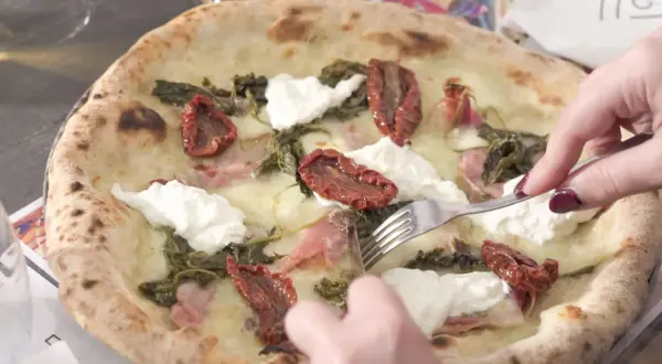 Una puccia Otranto, con pomodori secchi, burrata e verdure, viene tagliata con una forchetta.