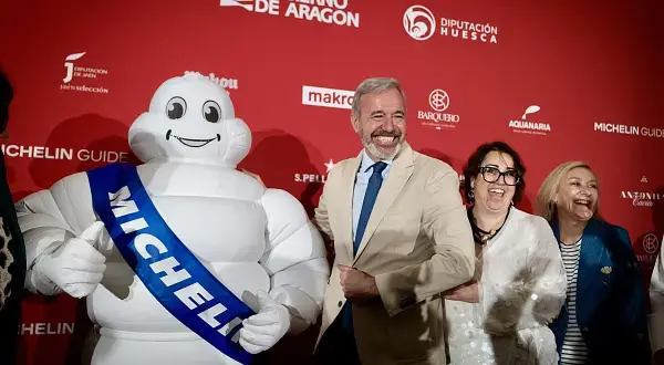 Bibendum, el muñeco Michelin, sonríe junto a autoridades en un evento que celebra la gastronomía de Huesca, destacando la **estrella Michelin Huesca**.