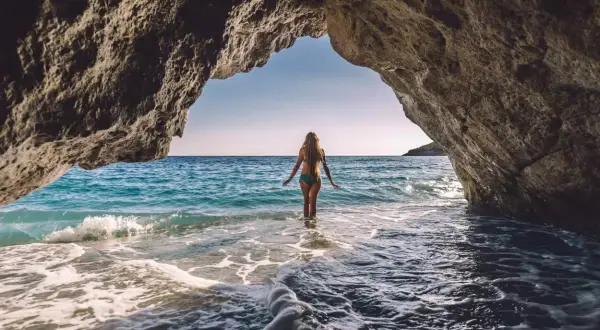 Kobieta wchodzi do turkusowej wody z jaskini. Idealne miejsce na wakacje all inclusive w Albanii.